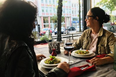 zwei Personen sitzen mit Essen an der offenen Fensterfront der Waschküche